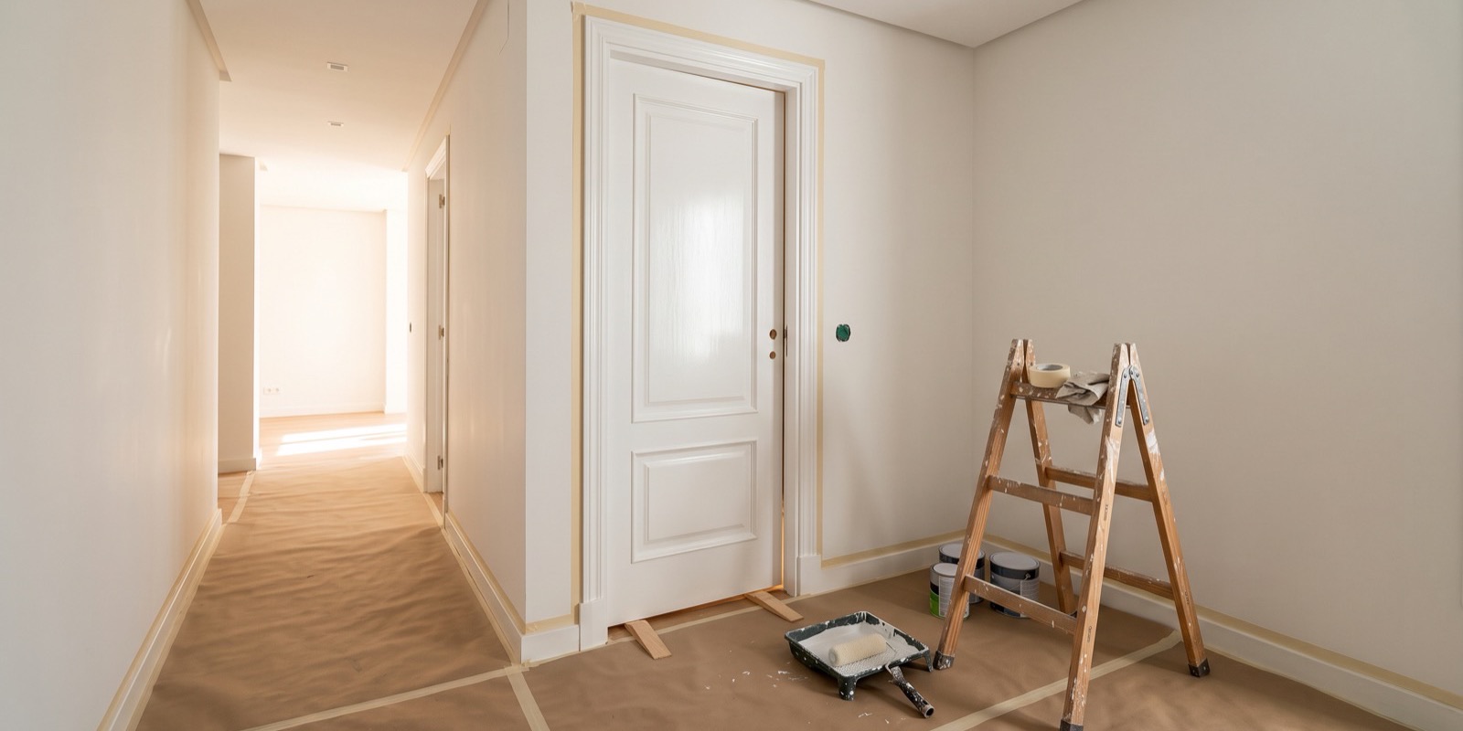 Puerta interior lacada en blanco en un piso de Madrid recién pintado, con escalera de madera de pintor, papel protector en el suelo y rodapiés enmascarados con cinta